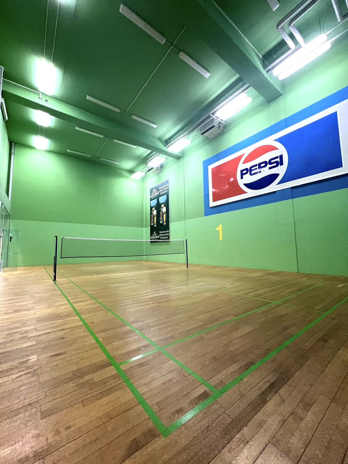 Badminton Court 1 mit gespanntem Badminton-Netz und Werbung an der Wand