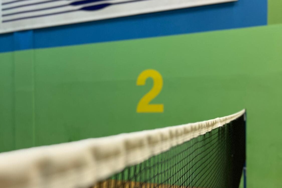 Ein Badminton-Netz vor grüner Wand mit der gemalten Nummer 2 als Kennzeichnung für den "Badminton Court 2"