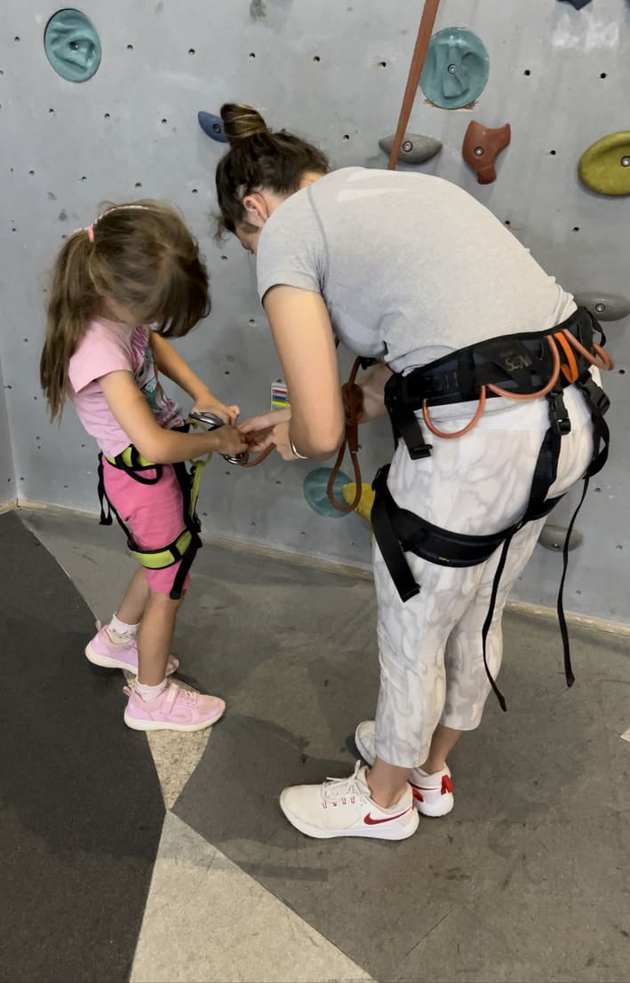 Eine Frau hilft einem Mädchen dabei, den Klettergurt anzulegen für das Kinderklettern im Sportcentrum