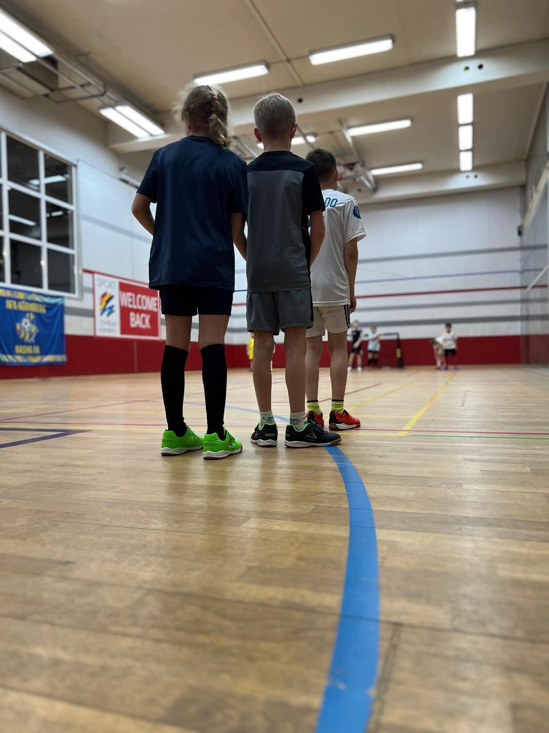 Drei Kinder stehen in Reihe hintereinander an für eine Sportübung beim Multisport Kindersport im Sportcentrum Nürnberg