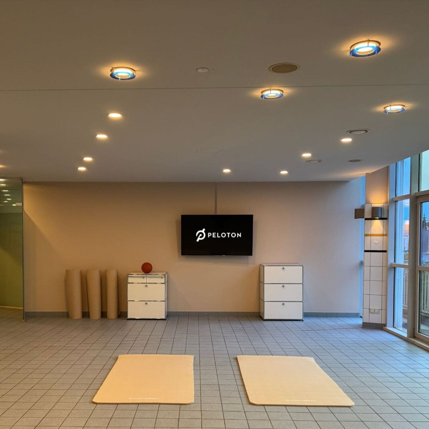 Kursraum mit Yogamatten ausgelegt und einem Fernseher, auf dem das Logo "Peloton" zu sehen ist im Sportcentrum Nürnberg