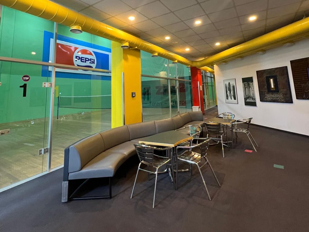 Lounge-Bereich mit Sitzgarnitur vor der Glaswand, die zum Badminton Court 1 führt