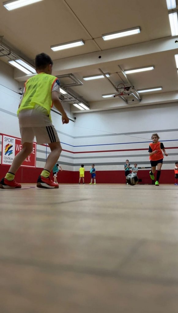 Ein Mädchen in orangenem Leibchen läuft auf einen Jungen im gelben Leibchen zu beim Multisport Kindersport im Sportcentrum Nürnberg