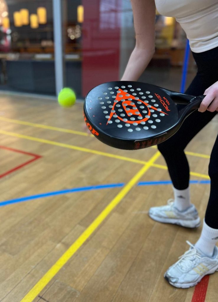 Tennisball springt vor einer Spielerin am Boden und sie ist bereit zum Aufschlag mit einem Padel Tennis-Schläger in der Hand.
