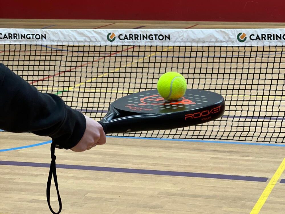 Tennisball liegt auf einem Padel Tennis-Schläger vor dem Tennisnetz im Sportcentrum Nürnberg