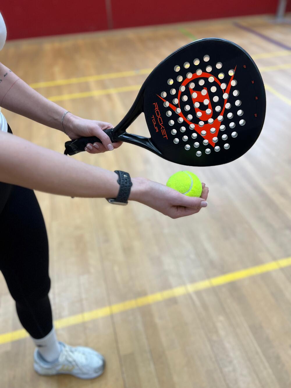 Tennisball liegt in der Hand einer Spielerin und ist bereit zum Aufschlag mit  einem Padel Tennis-Schläger in der anderen Hand.