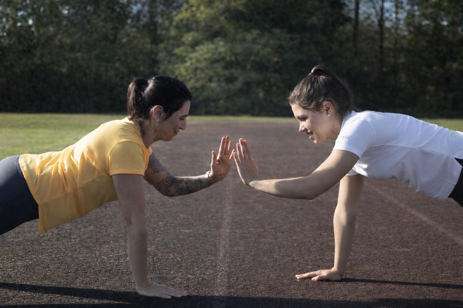 Zwei Frauen führen gemeinsam eine Sportübung aus, indem sie sich gegenüber in Liegestützposition jeweils eine Hand heben und einschlagen