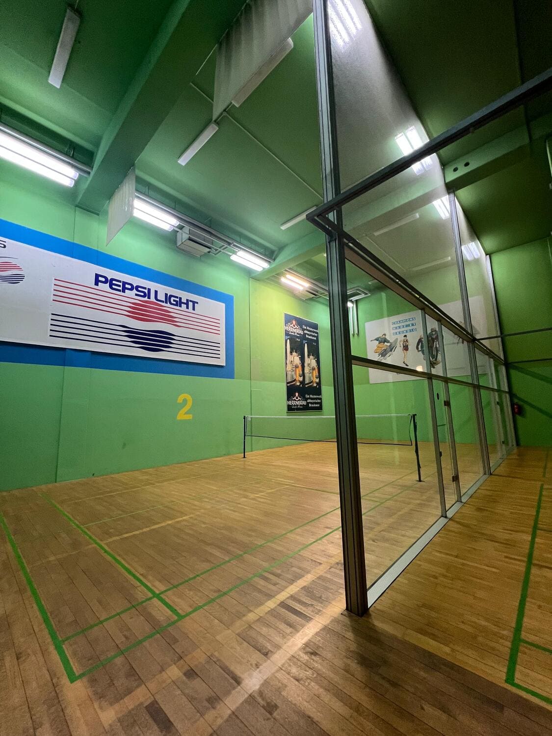 Das Badminton Court mit grünen Wänden und der Nummer 2 an der Wand mit gespanntem Badminton-Netz und gläserner Trennwand zum anderen Court im Sportcentrum Nürnberg