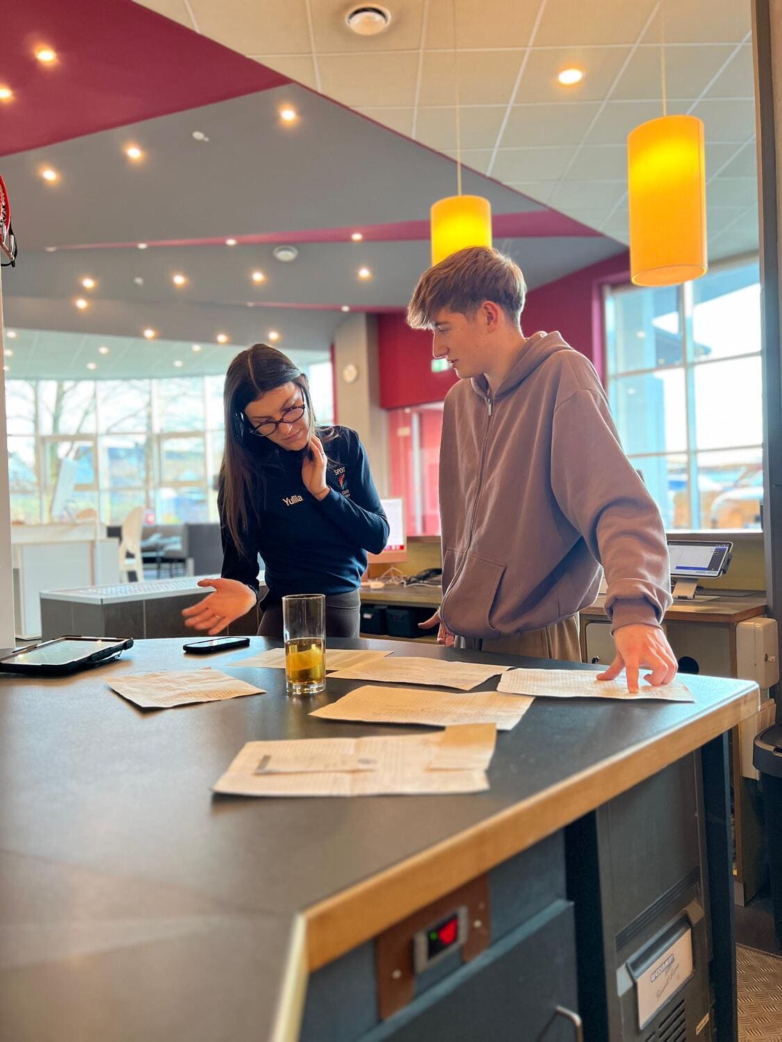 Ein junge Frau steht mit einem jungen Mann vor einem Tisch, auf dem verschiedene Pläne und Dokumente ausgelegt sind und sie betrachten diese gemeinsam