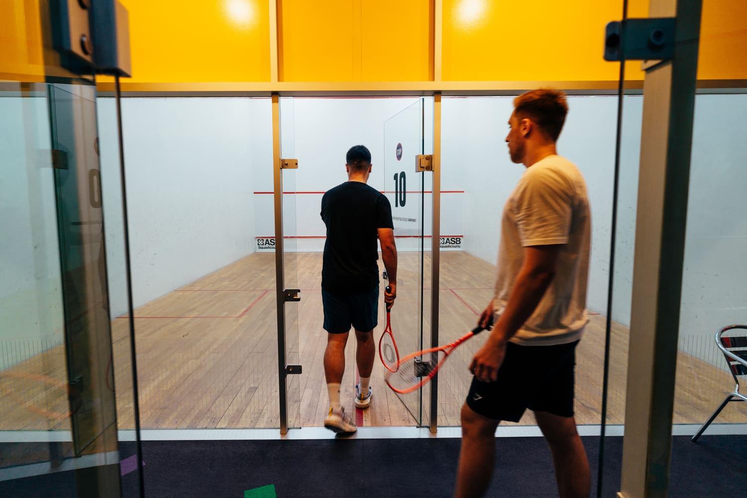 Zwei Männer gehen durch die Glastür mit dern Nummer 10 darauf in den Squash Court des Sportcentrums Nürnberg