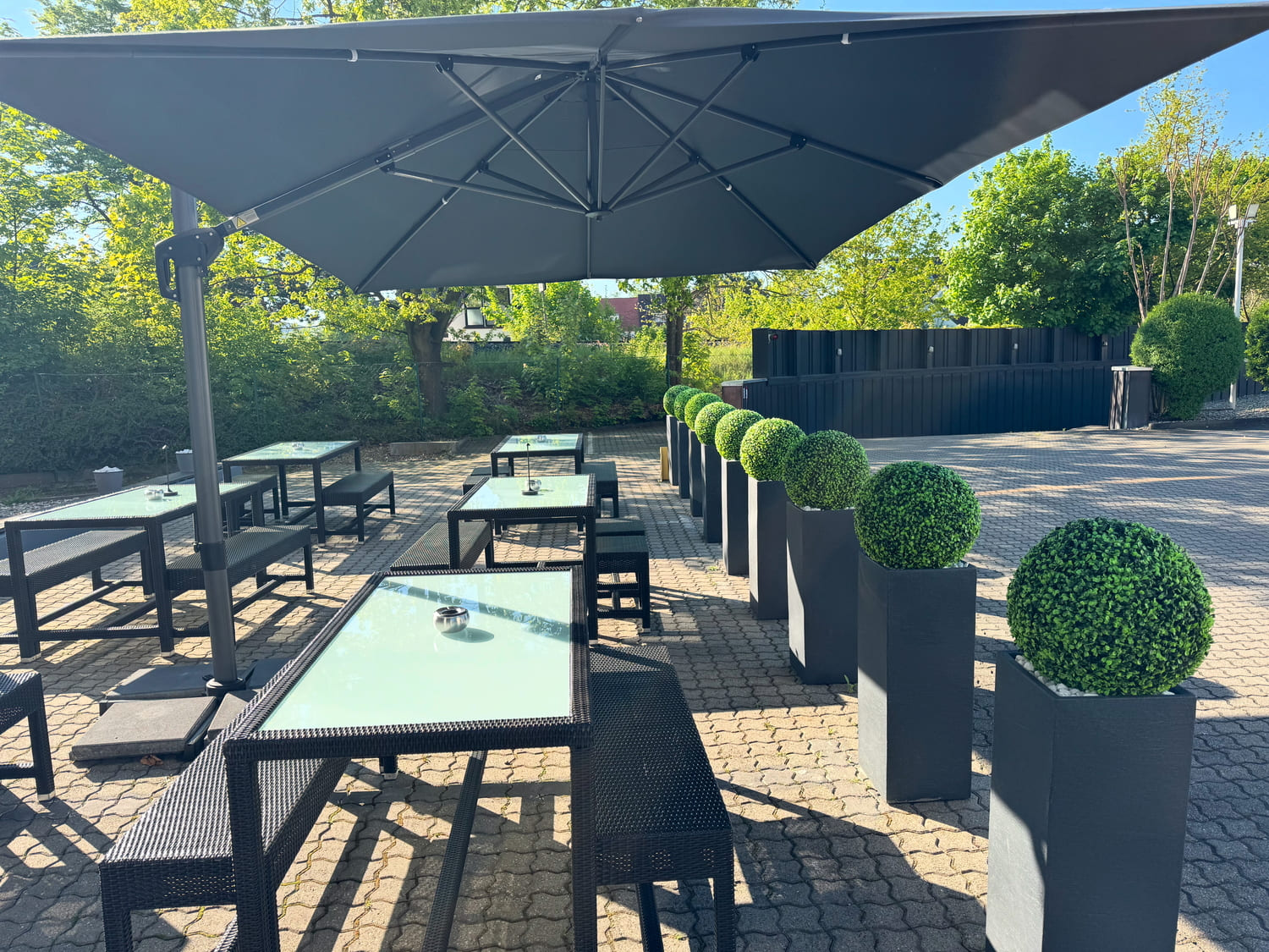 Außenbereich und Terrasse mit modernen Sitzbänken und Tischen unter einem dunklen Sonnenschirm vor dem Sportcentrum Nürnberg