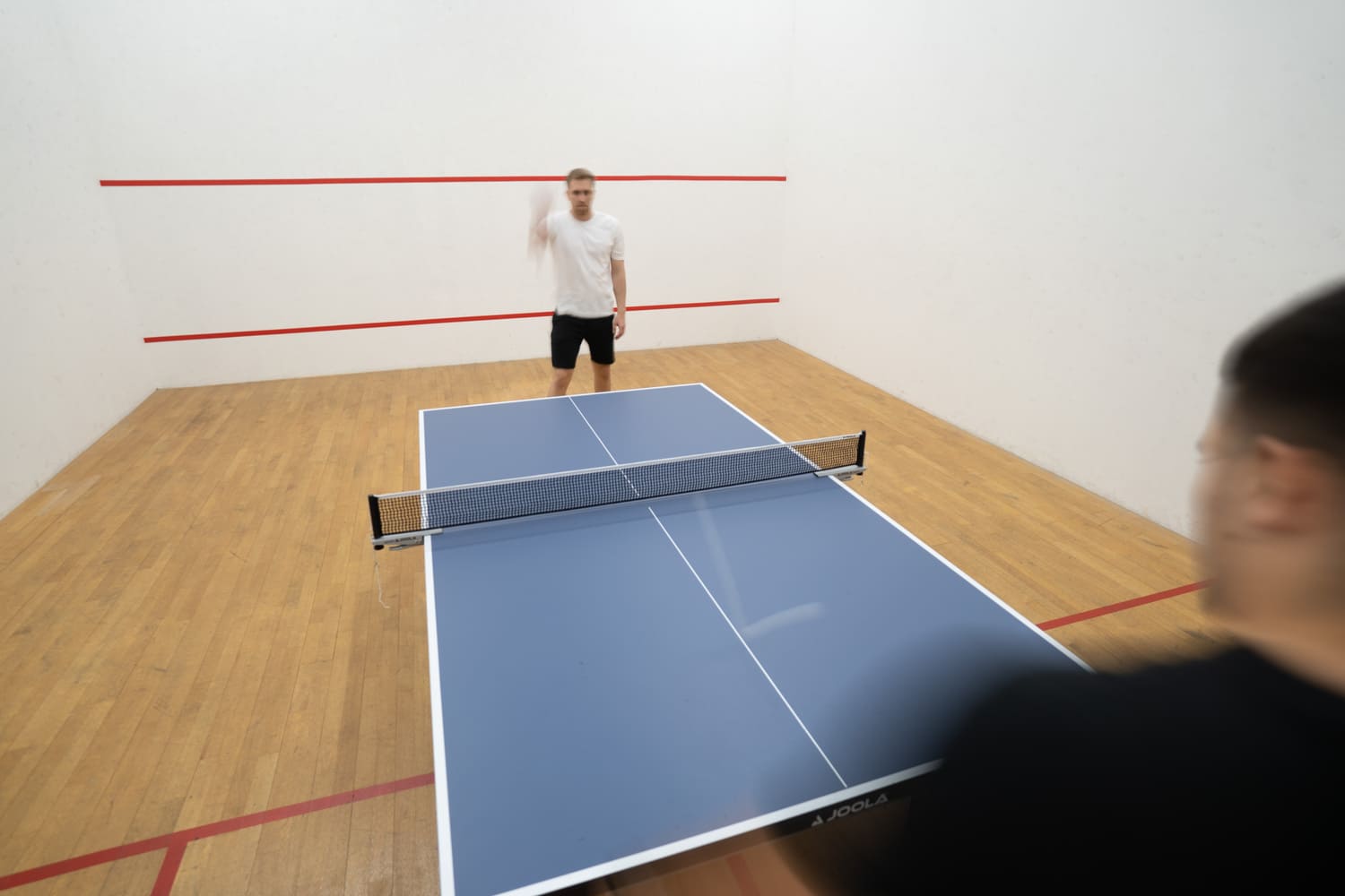 Ein Mann spielt einen Aufschlag beim Tischtennis und der Ball ist durch Langzeitbelichtung eine sichtbare Fluglinie über die Platte.