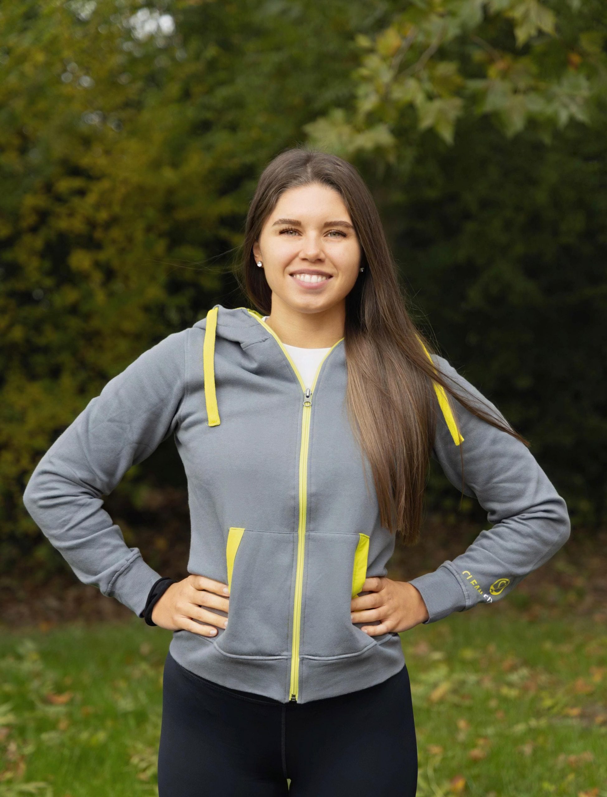 Die Personal Trainerin steht im Trainingsanzug vor der Kamera und lächelt. 