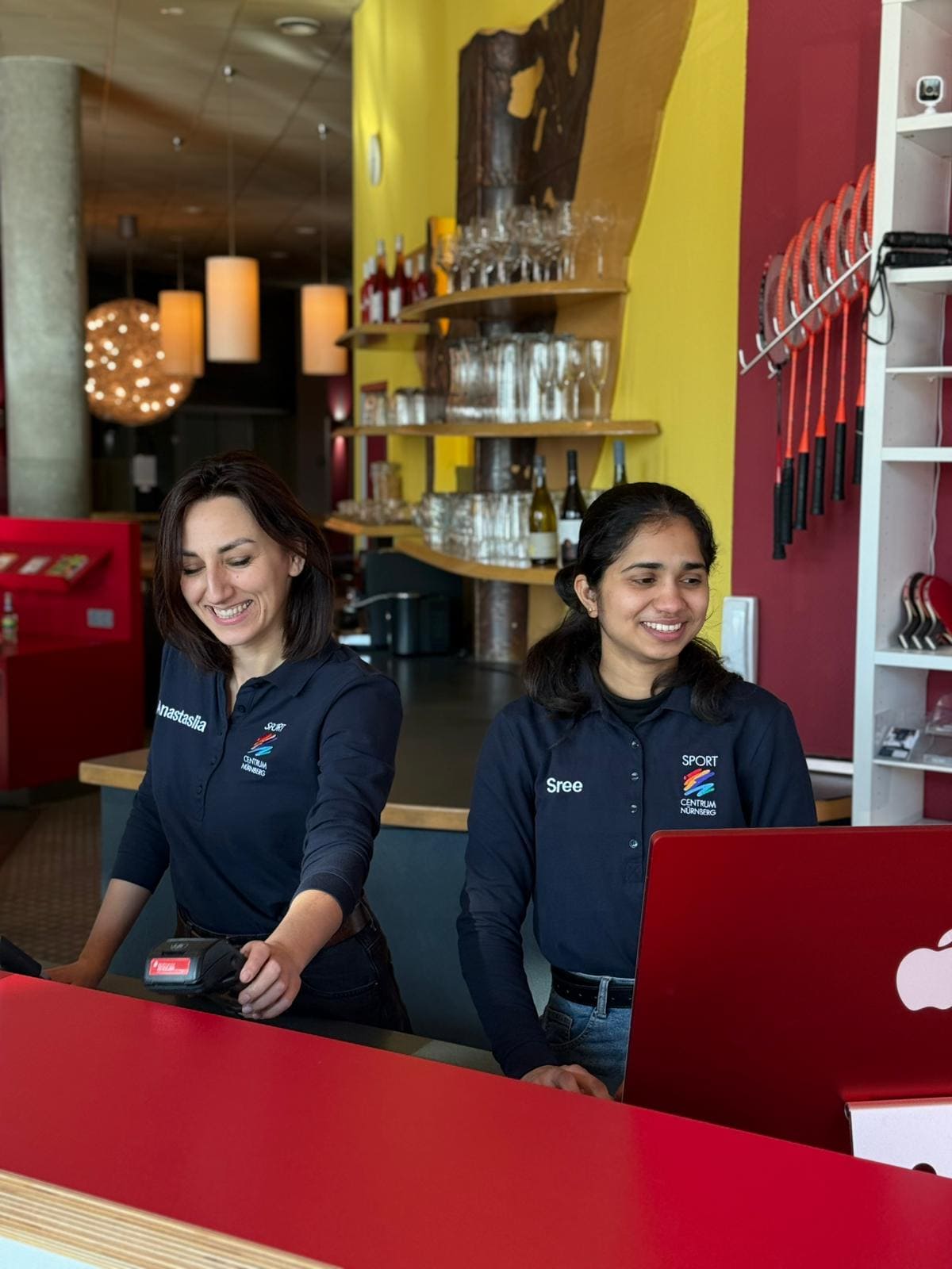 Zwei Mitarbeiterinnen des Sportcentrum Nürnberg stehen hinter der Empfangstheke und bedienen einen Kunden