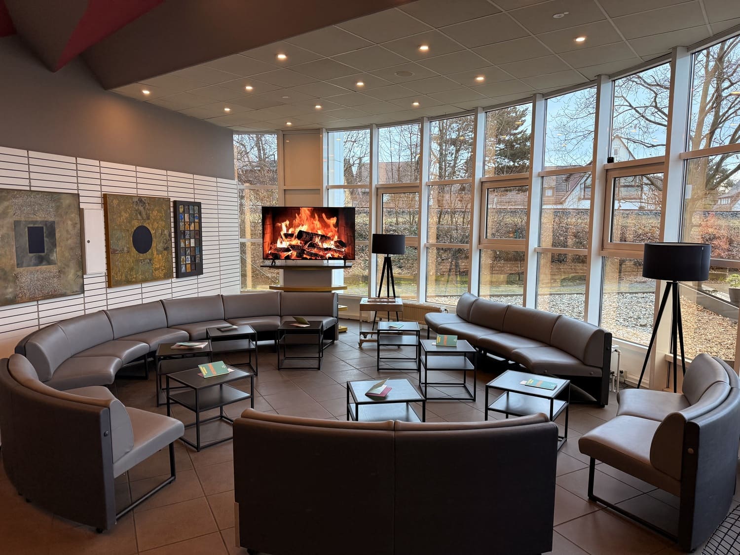 Gemütlicher Wartebereich der Lounge mit rundem Sitzbereich und einem Fernseher, auf dem ein Kaminfeuer läuft im Sportcentrum Nürnberg